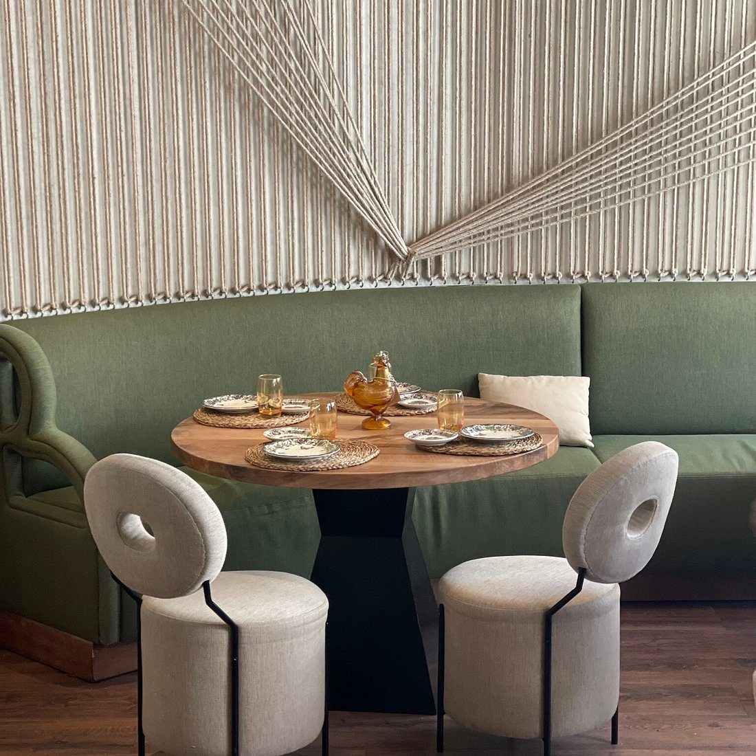 Sala de Coquetto: banco corrido verde, mesa redonda de mármol y taburetes tapizados en crudo, bajo un techo de listones de madera.