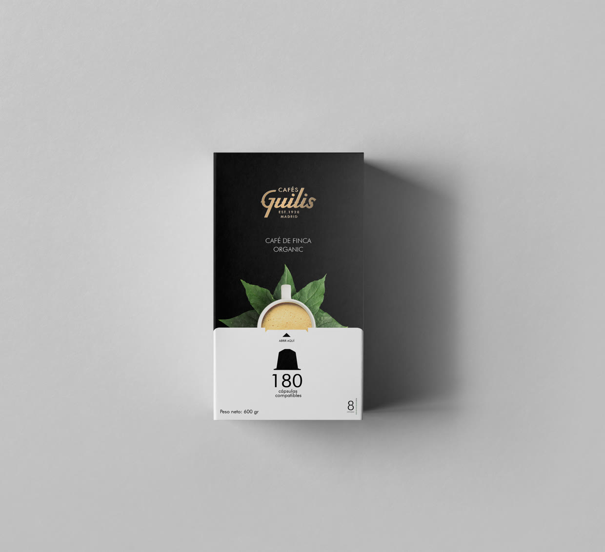 Cenital del estuche negro: Café de Finca Organic, con el logotipo en oro y una taza sobre hojas verdes.