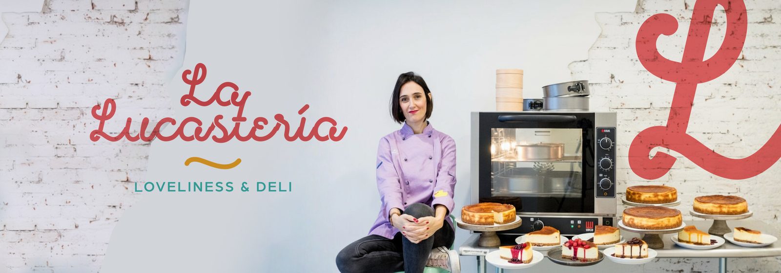 Banner de La Lucastería: el logotipo manuscrito rojo con «Loveliness & Deli» debajo, junto a una fotografía de María Lucas sentada delante de una fila de tartas de queso y un horno.
