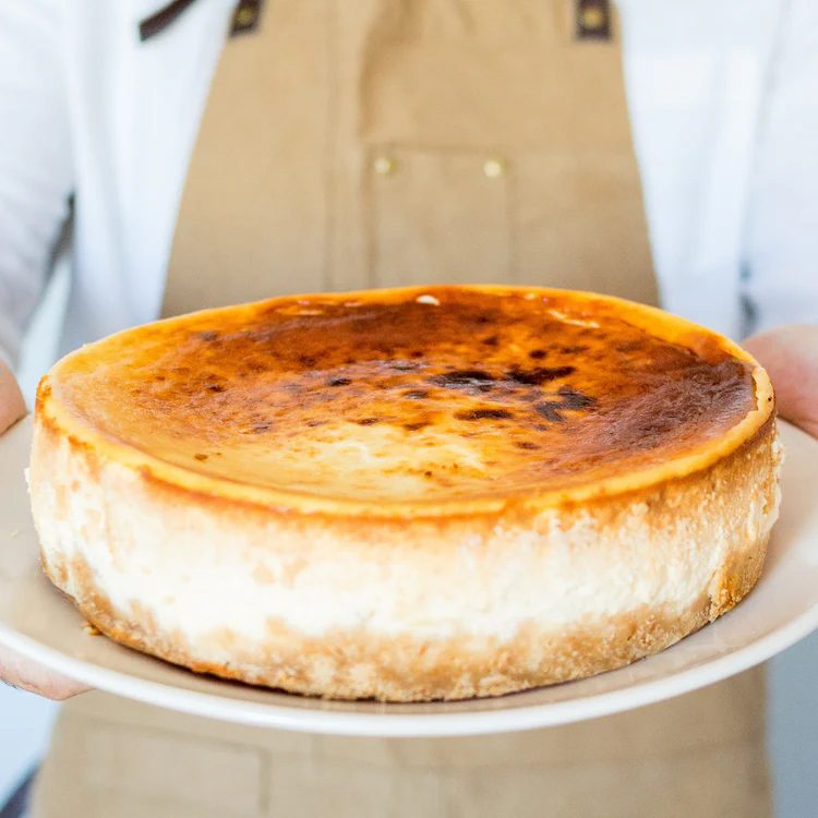 Tarta de queso clásica de La Lucastería, sostenida en un plato con la superficie tostada y cuarteada.