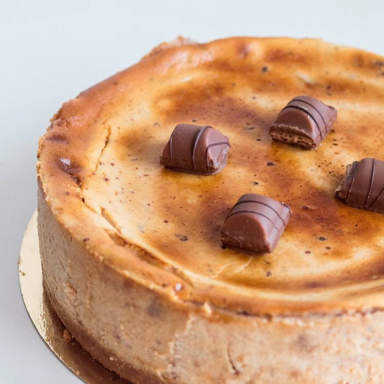 Tarta de queso de Kinder Bueno de La Lucastería, con trozos de la barrita repartidos sobre la superficie tostada.