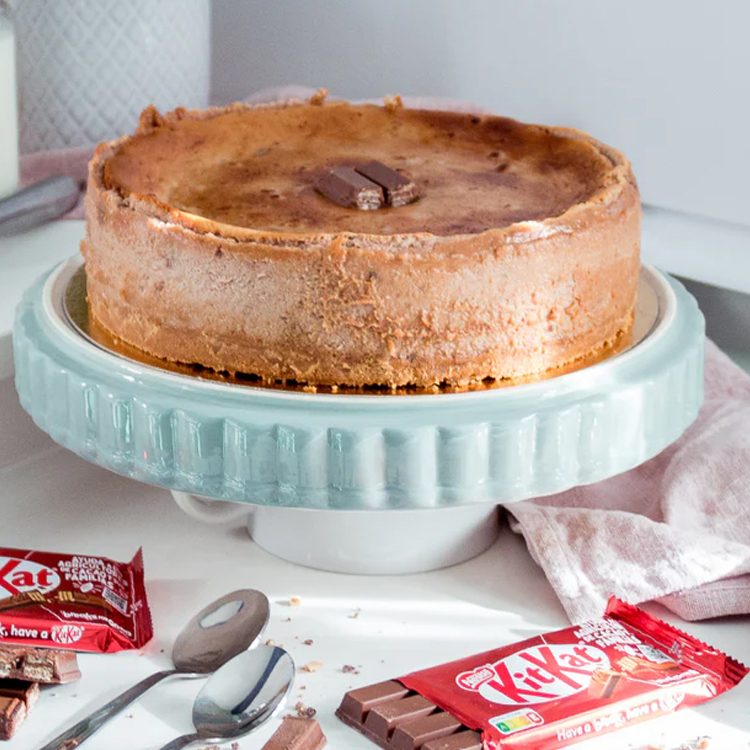 Tarta de queso de Kit Kat de La Lucastería sobre un pie de tarta verde menta, con barritas de Kit Kat alrededor.