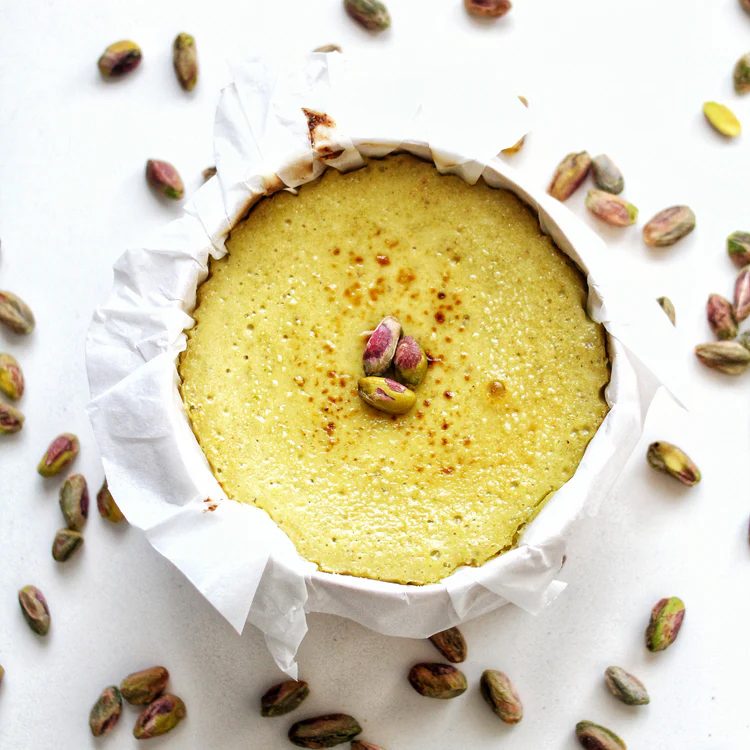 Tarta de queso de pistacho de La Lucastería, de color verde claro, rodeada de pistachos pelados sobre fondo blanco.