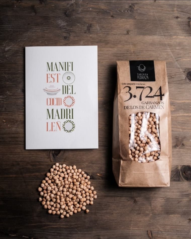 Sobre madera, el «Manifiesto del cocido madrileño» junto a una bolsa de «3.724 garbanzos de los de Carmen» y los garbanzos sueltos.